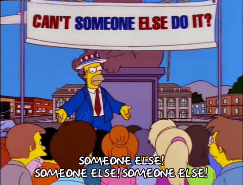 Homer Simpson leads a crowd in chanting the answer to all their problems (SOMEONE ELSE!)